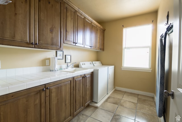 clothes washing area with washer and clothes dryer, sink, and cabinets