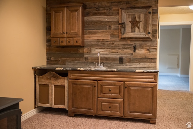 bar with dark stone counters, wooden walls, sink, and light carpet