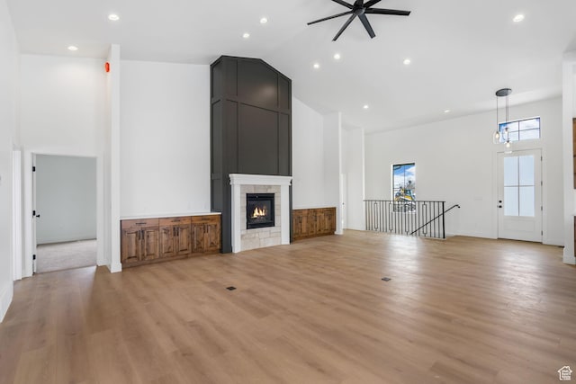 unfurnished living room featuring light wood-style floors, high vaulted ceiling, a ceiling fan, and a tile fireplace