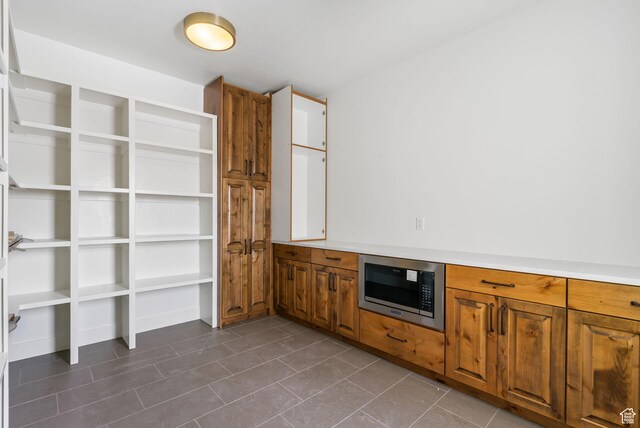 kitchen featuring brown cabinetry, stainless steel microwave, light countertops, and dark tile patterned floors