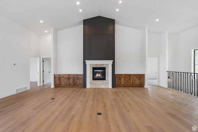 unfurnished living room with light wood-style flooring, a fireplace, visible vents, and high vaulted ceiling