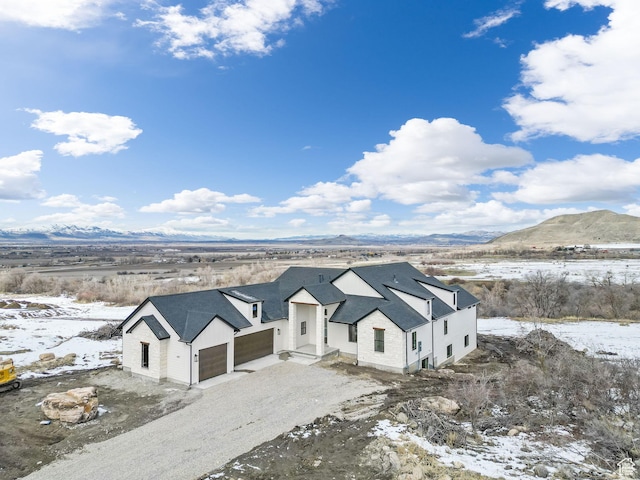 modern farmhouse style home featuring gravel driveway, an attached garage, and a mountain view