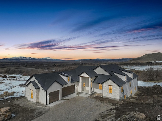 modern inspired farmhouse with an attached garage, a mountain view, dirt driveway, and roof with shingles