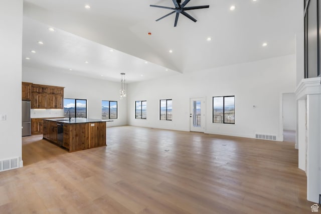 unfurnished living room with high vaulted ceiling, ceiling fan with notable chandelier, visible vents, and a sink