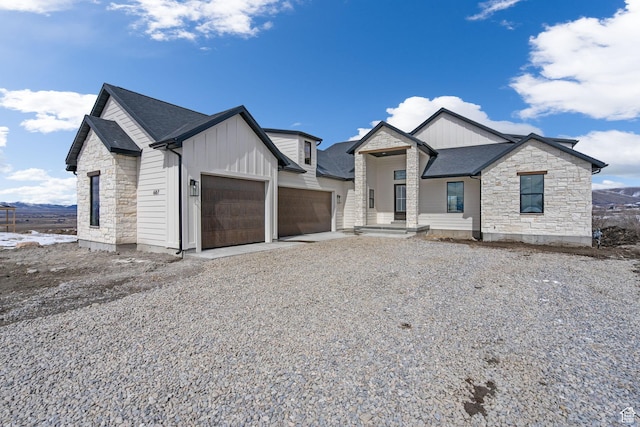 view of front of property featuring stone siding, an attached garage, a shingled roof, and gravel driveway