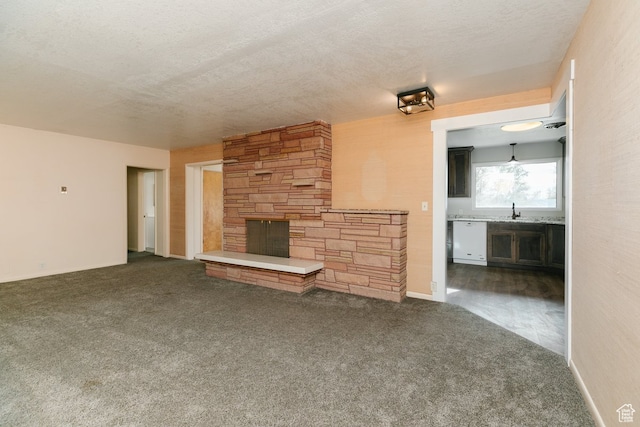unfurnished living room featuring dark colored carpet, a fireplace, sink, and a textured ceiling