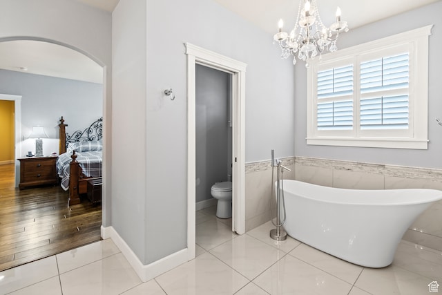 bathroom with a washtub, a notable chandelier, wood-type flooring, toilet, and tile walls