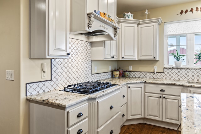 kitchen with decorative backsplash, white cabinets, light stone countertops, and gas stovetop