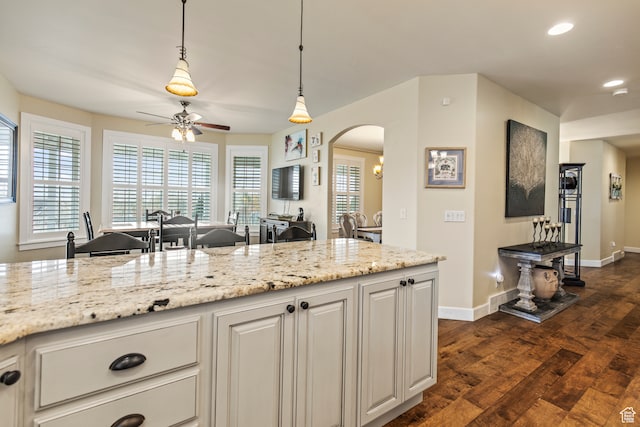 kitchen featuring ceiling fan, light stone counters, dark hardwood / wood-style flooring, pendant lighting, and white cabinets