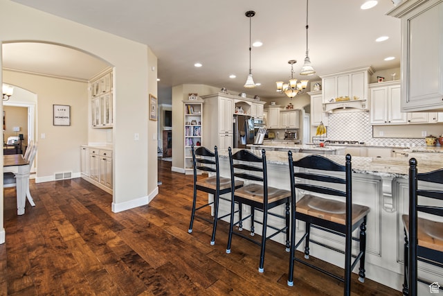 kitchen featuring dark wood-type flooring, a kitchen breakfast bar, light stone counters, a spacious island, and decorative light fixtures
