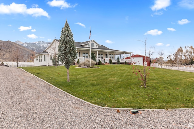farmhouse with a mountain view, a porch, a front lawn, a garage, and an outdoor structure