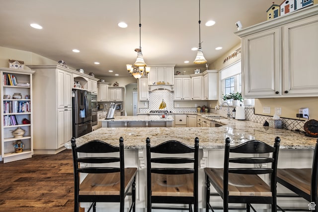 kitchen featuring light stone countertops, a breakfast bar, dark wood-type flooring, pendant lighting, and stainless steel refrigerator