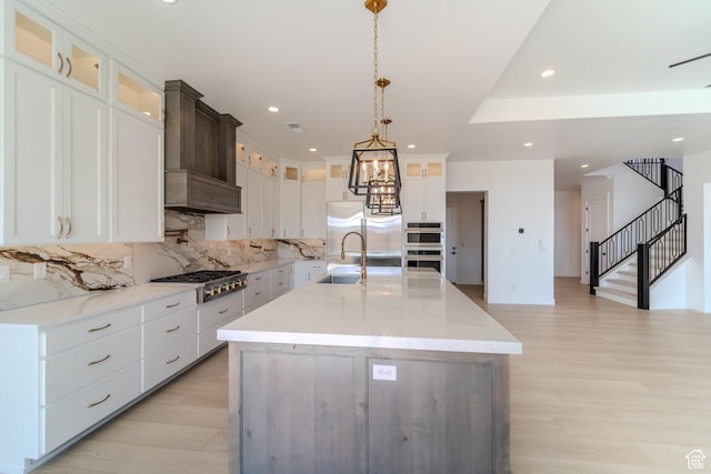 3092 E 2110th St S, St George, UT 84790 - kitchen featuring appliances with stainless steel finishes, a sink, backsplash, light wood-style flooring, and a center island with sink