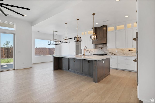 3092 E 2110th St S, St George, UT 84790 - kitchen featuring light countertops, white cabinets, decorative backsplash, a center island with sink, and light wood finished floors