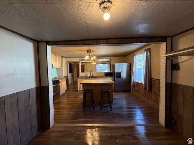 kitchen with brick wall, a kitchen island, appliances with stainless steel finishes, dark hardwood / wood-style floors, and a breakfast bar area