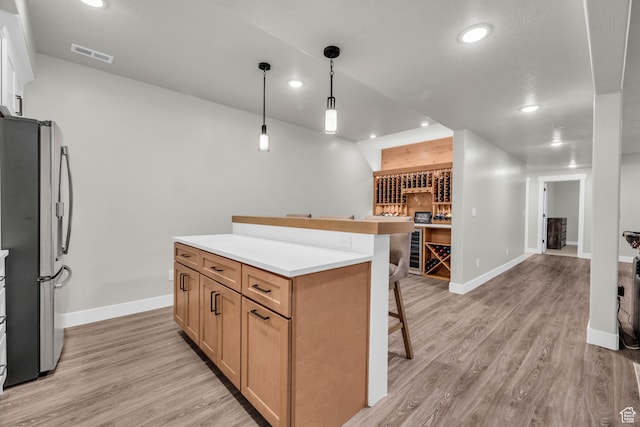 kitchen featuring pendant lighting, light hardwood / wood-style floors, a kitchen island, a kitchen bar, and stainless steel refrigerator