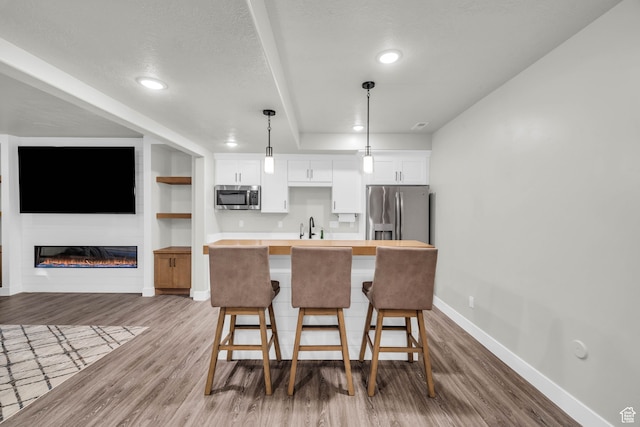 kitchen featuring pendant lighting, hardwood / wood-style floors, white cabinets, appliances with stainless steel finishes, and a kitchen bar