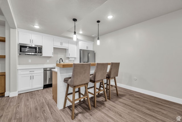 kitchen with pendant lighting, white cabinetry, stainless steel appliances, and light hardwood / wood-style flooring