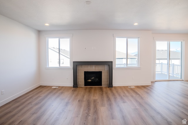 unfurnished living room featuring a tile fireplace, a wealth of natural light, light hardwood / wood-style floors, and a textured ceiling