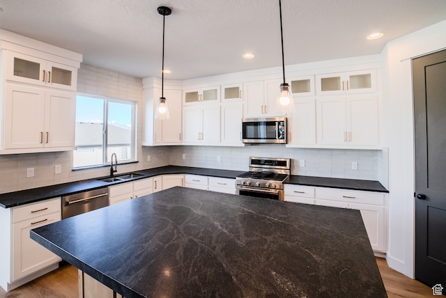 kitchen featuring appliances with stainless steel finishes, decorative light fixtures, white cabinetry, and sink