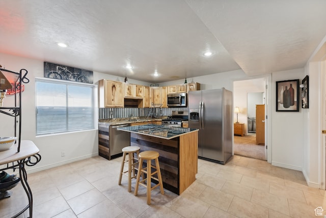 kitchen with light brown cabinetry, appliances with stainless steel finishes, a kitchen breakfast bar, backsplash, and a center island