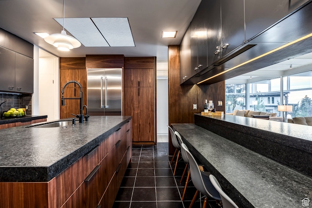 4345 S Zarahemla Dr, Salt Lake City, UT 84124 - kitchen with built in fridge, dark tile patterned flooring, sink, decorative backsplash, and an island with sink