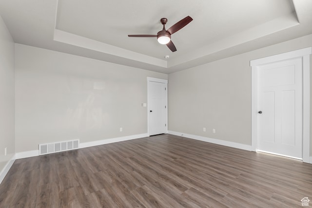 spare room with a tray ceiling, ceiling fan, and dark hardwood / wood-style flooring