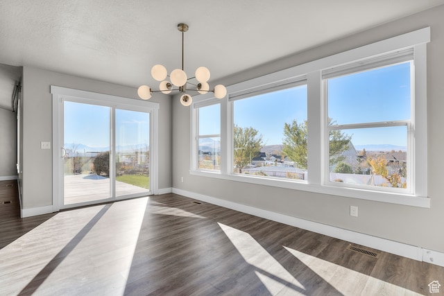 unfurnished dining area featuring a notable chandelier, dark hardwood / wood-style flooring, a mountain view, and a textured ceiling