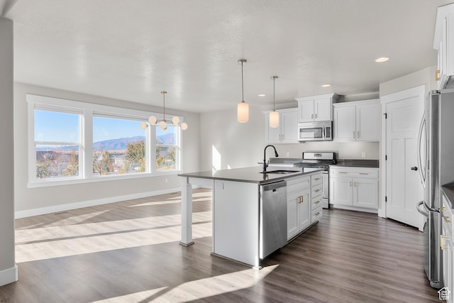kitchen with dark wood-type flooring, decorative light fixtures, a center island with sink, white cabinets, and appliances with stainless steel finishes