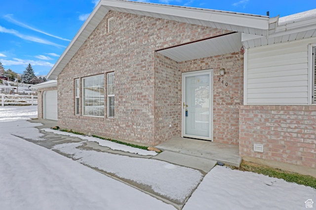 snow covered property entrance featuring a garage