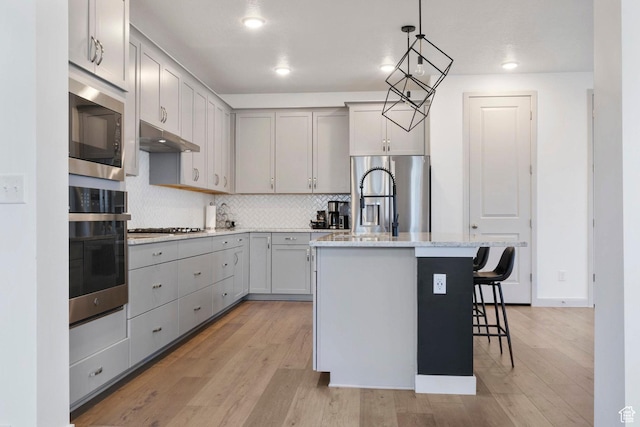 kitchen featuring a breakfast bar area, hanging light fixtures, a center island with sink, appliances with stainless steel finishes, and gray cabinets
