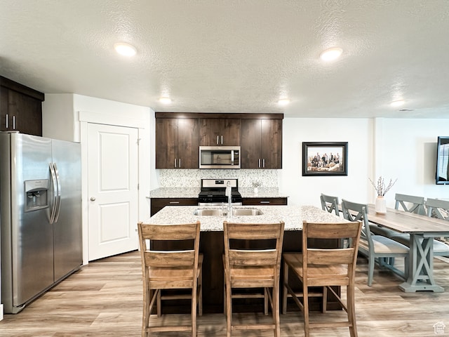 kitchen featuring dark brown cabinets, an island with sink, stainless steel appliances, and a textured ceiling