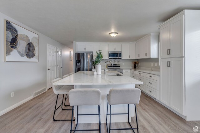 kitchen featuring light wood-type flooring, stainless steel appliances, a kitchen island with sink, sink, and white cabinets