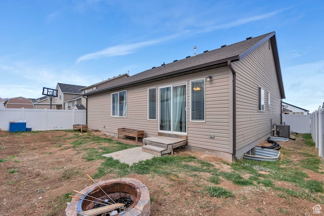 rear view of property featuring a lawn, central AC unit, and a fire pit