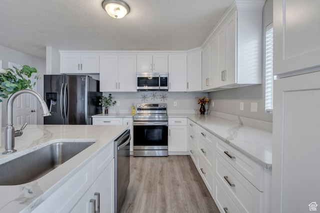 kitchen with white cabinets, light stone counters, light wood-type flooring, and appliances with stainless steel finishes