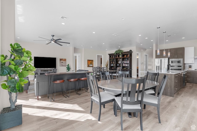dining space with ceiling fan, light hardwood / wood-style floors, and sink