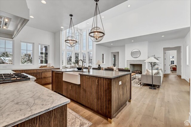 kitchen with sink, light wood-type flooring, an island with sink, range hood, and a chandelier