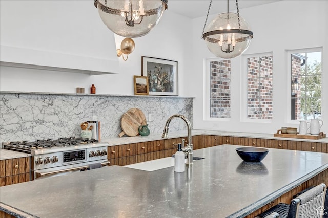 kitchen featuring decorative backsplash, high end stove, sink, decorative light fixtures, and a chandelier