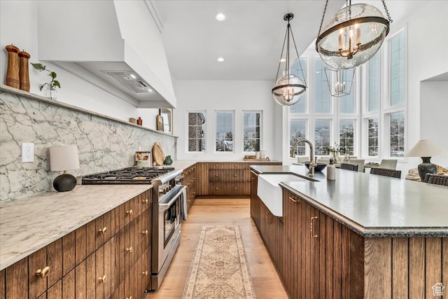 kitchen with sink, high end stainless steel range oven, an inviting chandelier, pendant lighting, and light wood-type flooring
