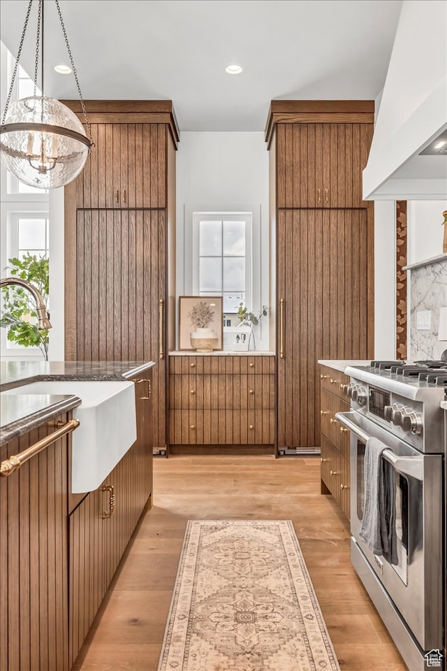kitchen featuring tasteful backsplash, a notable chandelier, high end stove, light hardwood / wood-style floors, and custom exhaust hood