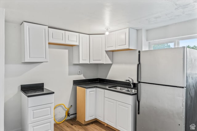 kitchen with white cabinetry, stainless steel refrigerator, light hardwood / wood-style floors, and sink