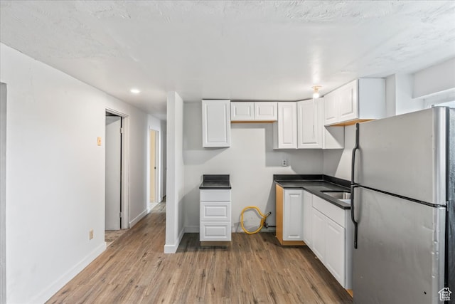 kitchen featuring stainless steel refrigerator, light hardwood / wood-style flooring, white cabinets, and a textured ceiling