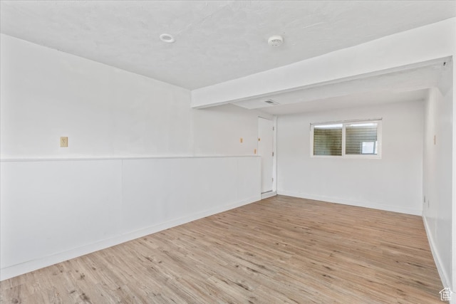 spare room featuring beamed ceiling and light wood-type flooring