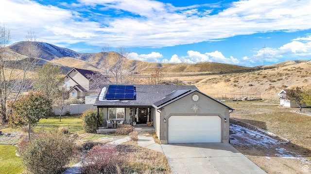 10877 N Wallace Ln E, Tremonton, UT 84337 - view of front of house with covered porch, driveway, roof mounted solar panels, an attached garage, and a mountain view