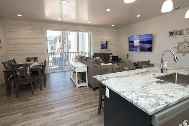 kitchen with light stone countertops, sink, dark hardwood / wood-style floors, an island with sink, and wooden walls