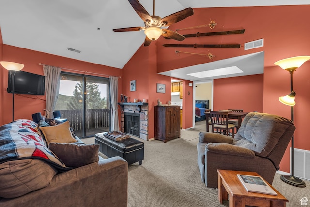 living room featuring light carpet, a skylight, ceiling fan, high vaulted ceiling, and a stone fireplace