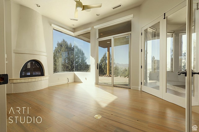 unfurnished living room with wood-type flooring, a large fireplace, and ceiling fan