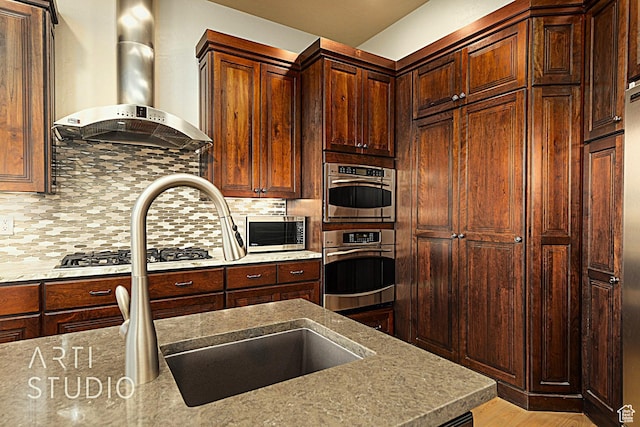 kitchen with wall chimney exhaust hood, stainless steel appliances, light hardwood / wood-style floors, and decorative backsplash