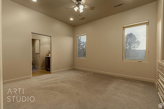 unfurnished bedroom with multiple windows, connected bathroom, light colored carpet, and ceiling fan