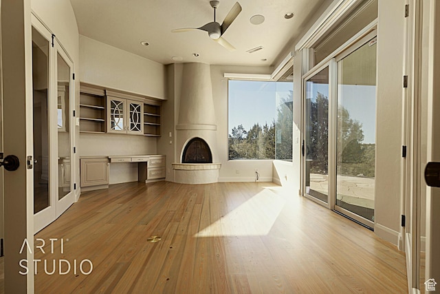 unfurnished living room featuring built in desk, a fireplace, ceiling fan, and light hardwood / wood-style flooring